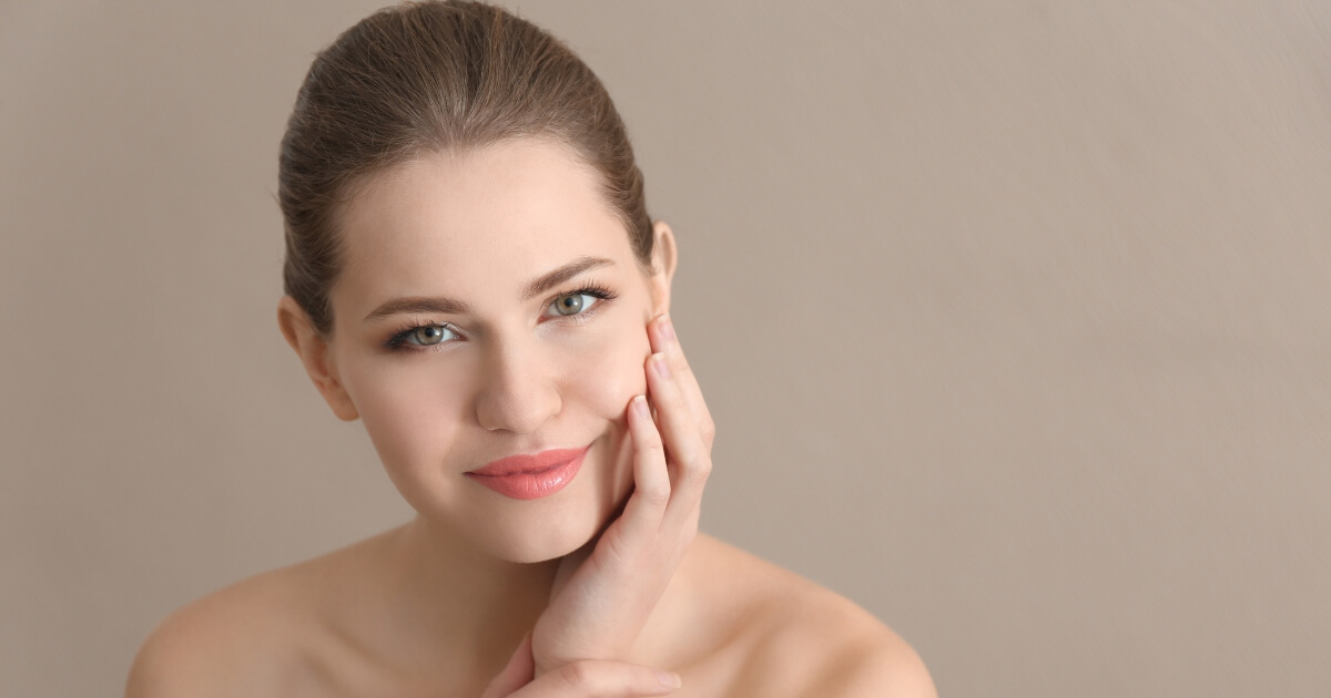 A young woman with a flawless skin and brown hair smiling softly.